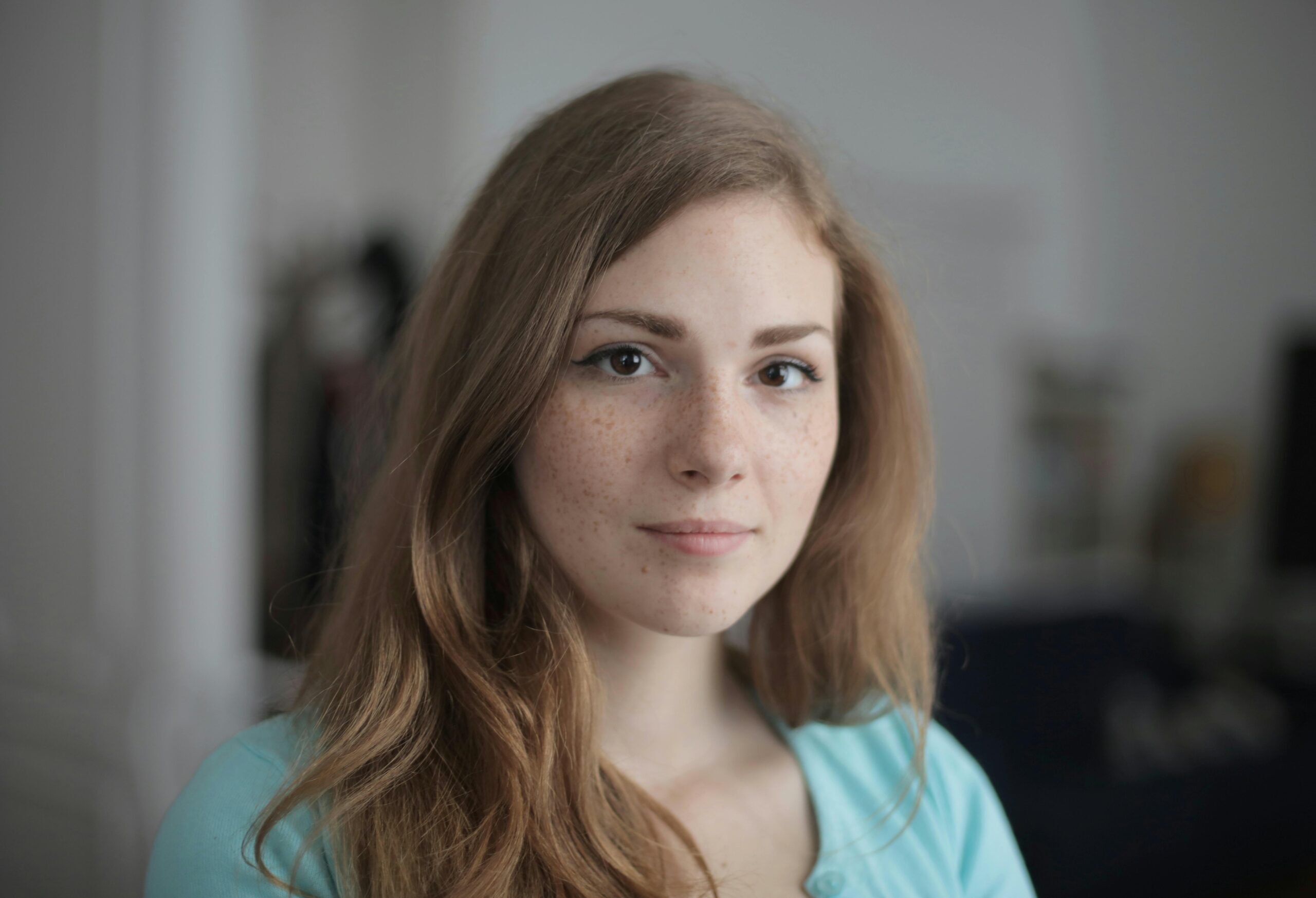 Close-up portrait of a young freckled woman indoors, expressing calm and beauty.